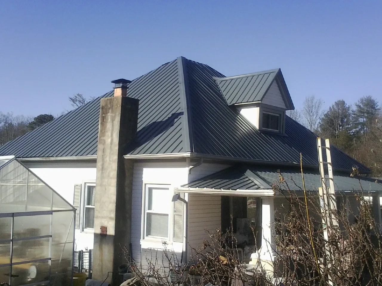 Dark blue standing seam metal roof on a white farmhouse with dormer — Slate & Tile Roof Repair by Roofing Brothers in Redvale