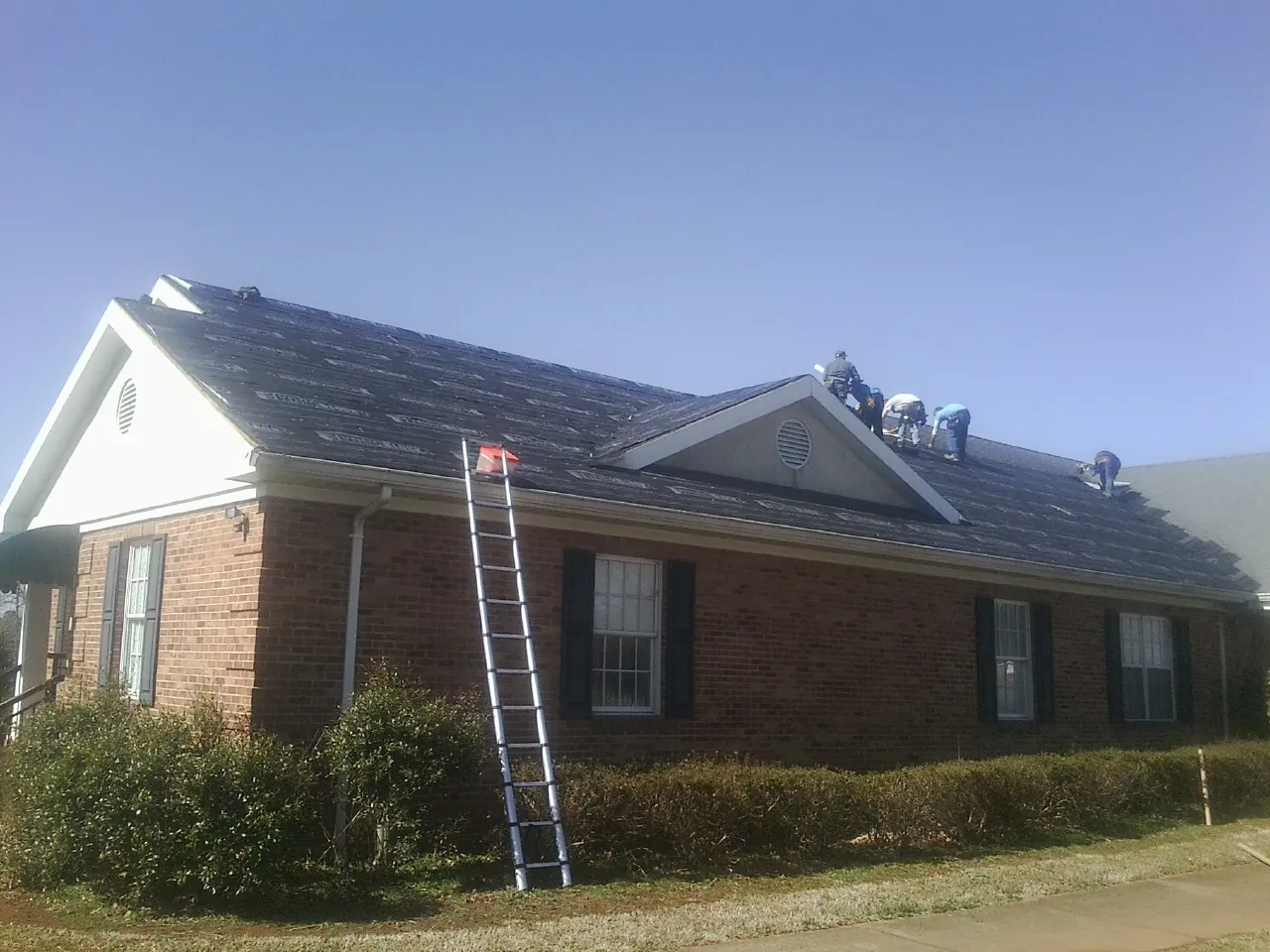 Crew tearing shingles off a brick ranch roof with a ladder set — Emergency Roof Repair work by our crew in Redvale