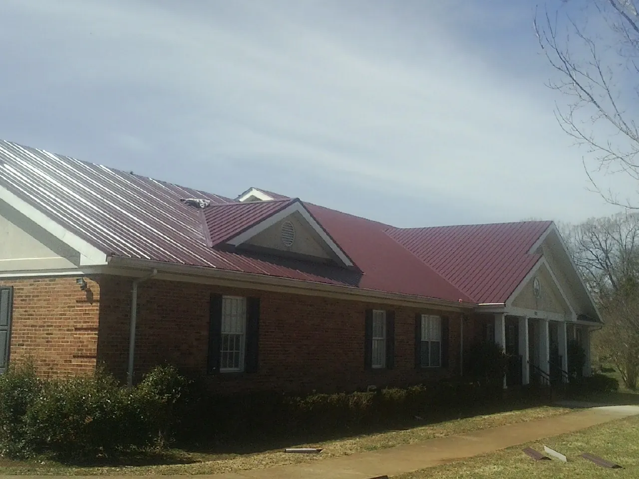 Red metal roof with gabled entries on a long brick building, from a Hail Damage Roof Repair job in Redvale