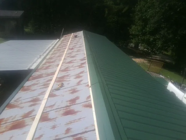 Old rusted panels beside newly installed green metal roofing — Wind Damage Roof Repair by Roofing Brothers in Redvale
