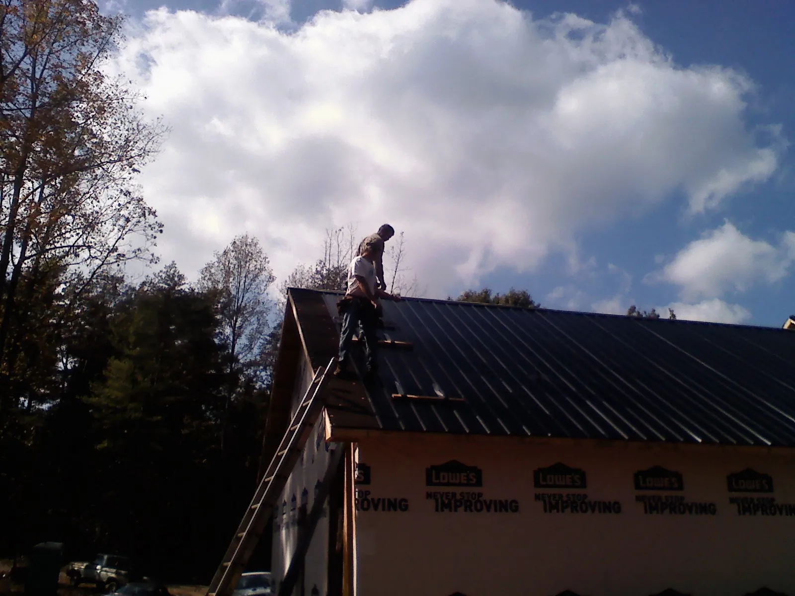 Roofer fastening dark metal panels high against a cloudy sky, from a Roof Inspection job in Redvale